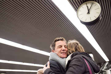 Wall Mural - Senior couple standing at the underground platform, hugging