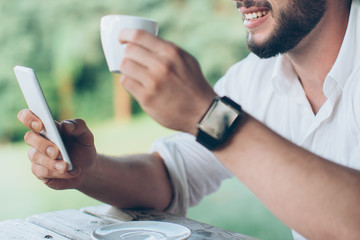 Close up of a young man using mobile phone and drinking coffee