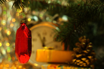 Christmas and New Year`s vintage clock showing five to midnight. Gold gift box with gold bow, retro toy red glass ruby crystal, fir cones and tree branches. Greeting card Background for holiday.