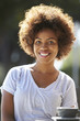 © Monkey Business - Happy young black woman sitting outside a cafe, vertical