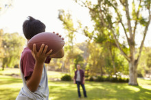 Young Boy Throwing Ball To Dad In Park, Focus On Foreground