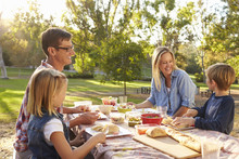 Young White Family Enjoying A Picnic At A Table In A Park