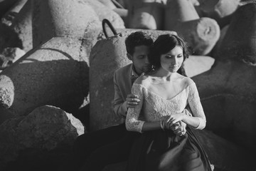 Romantic and stylish caucasian couple hugging at sunrise near the sea bay. Black and white image.