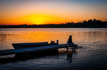 Tranquil Silhouette Of Woman Sitting On The Dock On The Shore Of A Calm Lake In Minnesota