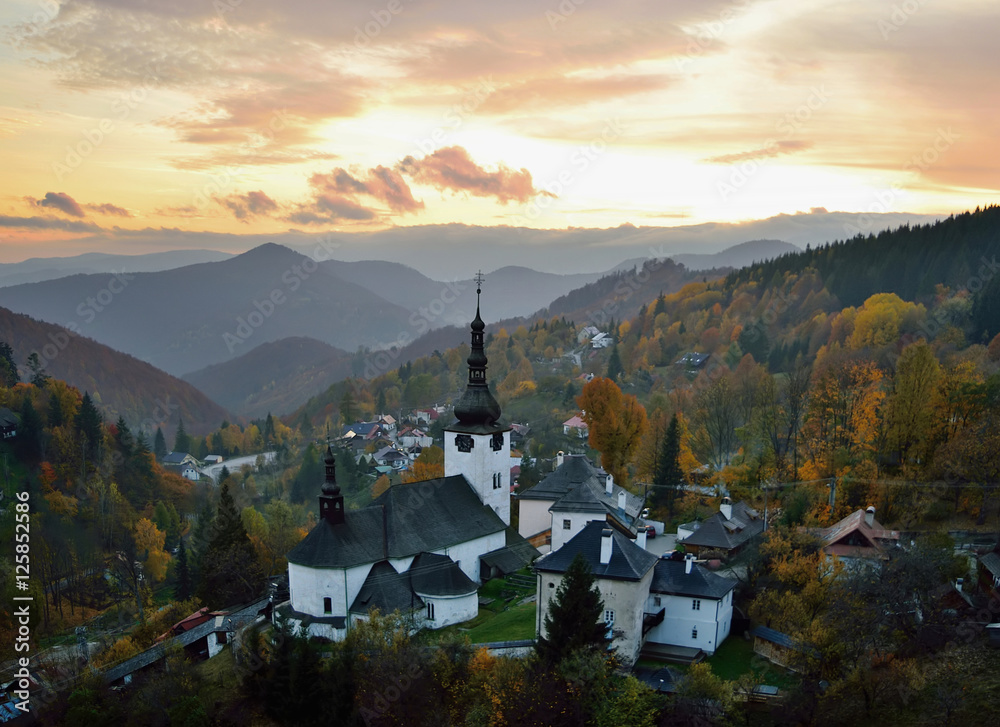 Fall in Slovakia. Old mining village. Historic church in Spania dolina. Autumn colored trees at sunset. - obrazy, fototapety, plakaty 