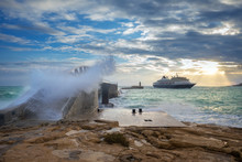 Valletta, Malta - Amazing, Huge Waves Over The Breakwater Bridge At Valletta's Entrance With Cruise Ship And Sunrise At Background