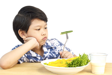 Asian lovely boy showing boring expression with fresh colorful vegetables and glass of milk isolated over white background