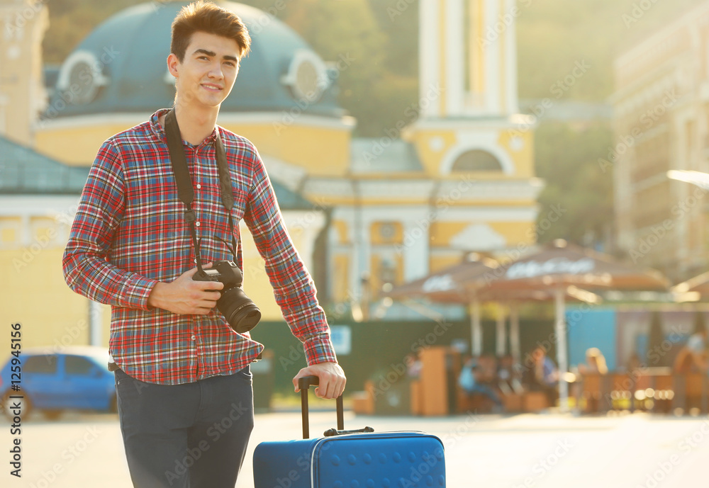 Young man with big blue trunk and camera standing on the street