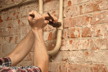 Closeup Hands Of A Plumber At Work Holding A Pipe Wrench, Plumber Fixing A Leak In The Basement, Red Brick Background (with Copyspace)