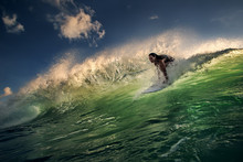 A Surfer Girl Riding Inside An Ocean Green Wave Lit With Sunset Light. Watersport Activity In Indonesian Island Bali. Green Water With Blue Dark Sky.