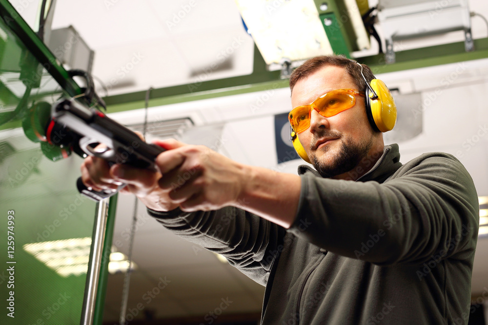 Nauka posługiwania się bronią palną. Mężczyzna na strzelnicy przeładowuje pistolet - obrazy, fototapety, plakaty 