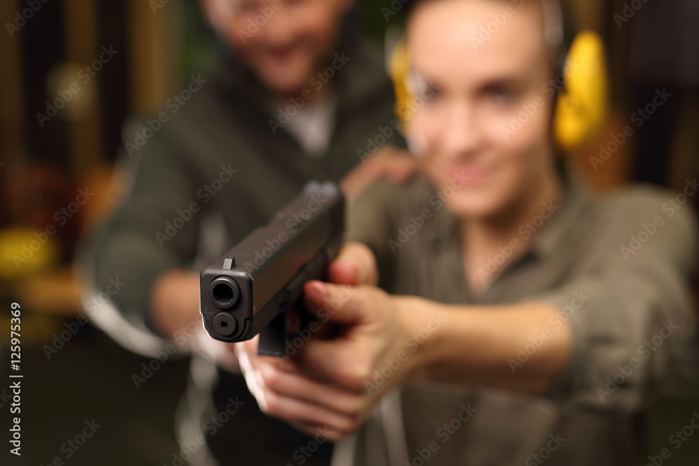 Kobieta z bronią. Kobieta bierze lekcje strzelania z broni krótkiej na strzelnicy sportowej - obrazy, fototapety, plakaty 