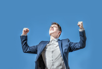 Triumphant business man rising his arms over blue sky background