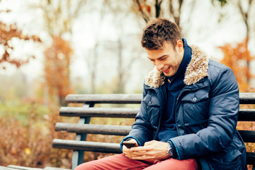 Handsome man sitting on bench and texting