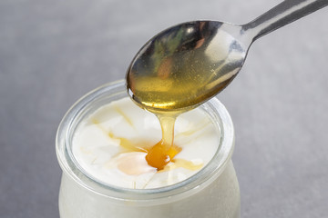 Yogurt and pouring honey on white background