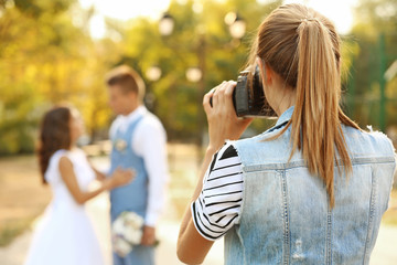 Wall Mural - Young woman taking photo of happy wedding couple in park