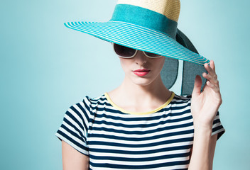 Female fashion model posing in studio wearing hat against a green turquoise background. 
