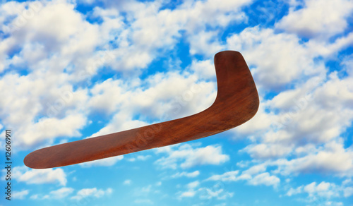 Fotomural Wooden australian boomerang in flight against of cloudy blue sky.