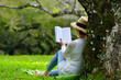 © amenic181 - Middle aged woman sitting under a tree reading a book in the park