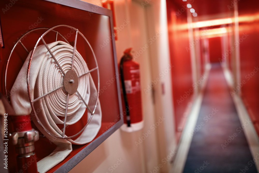 Fire extinguisher and hose reel in hotel corridor - obrazy, fototapety, plakaty 
