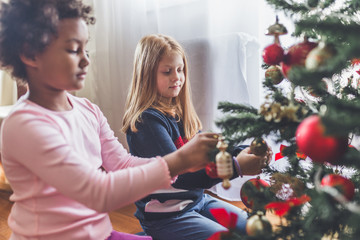 African and redhead little girls decorating the Christmas tree. Natural light. 