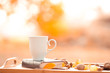 © morrowlight - White cup of tea staying on book with nuts and yellow leaves on wooden tray outdoors.