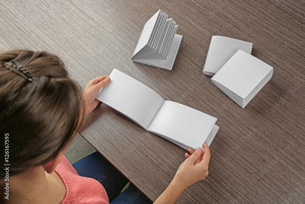 Woman sitting at wooden table with blank brochures