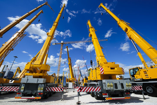 mobile construction cranes with yellow telescopic arms and big tower cranes in sunny day with white 