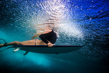 Wall Mural - slim blonde girl in bikini a surfer with surf board duck diving underwater under ocean reflected sur