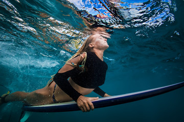 Wall Mural - slim blonde girl in bikini a surfer with surf board duck diving underwater under ocean reflected sur