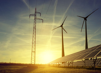 Wall Mural - electricity transmission pylon with solar panels and wind turbines on field against the sunset.