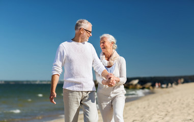 Wall Mural - happy senior couple holding hands on summer beach