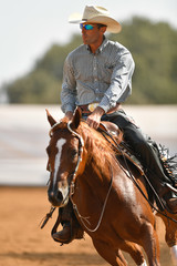 Wall Mural - The front view of a rider in cowboy chaps, boots and hat on a horseback running ahead