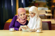 Two Muslim women in a cafe, shop online using electronic tablet