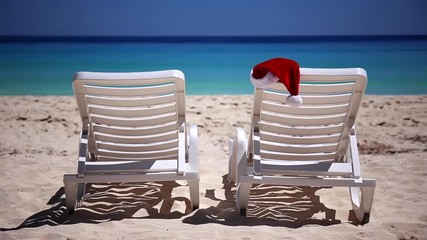 Wall Mural - Santa Claus Hat on sunbed near  tropical calm beach with turquoise caribbean sea water and white sand. Christmas vacation concept