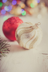 Two christmas bauble close up on the off white wooden table with the lights on the back; selective focus. Photo with applied vintage filter; toned photography