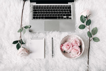 Freelance woman workspace in flat lay style with laptop, vintage tray, roses, notebook and pen on white fur background. Top view, flat lay. Freelance concept.