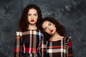 Pretty sisters twins posing looking at camera over grey background.