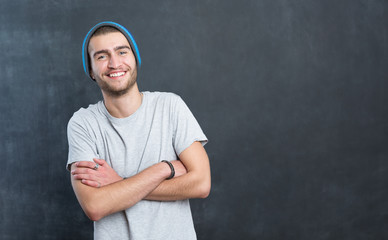 Happy young man standing with arms crossed over blackboard backg