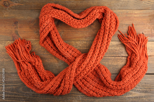 Fotografie, Obraz Knitted orange scarf in the shape of a heart on a wooden background