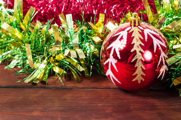 Christmas red ball with reflection. Wooden table and tinsel in the background.