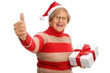 Cheerful Senior Holding Christmas Present And Giving Thumb Up