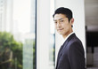 © Mint Images - A businessman in the office, by a large window, looking at the camera.