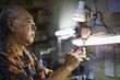 © Mint Images - A senior craftsman at work in a glass maker's studio workshop, in inspecting red wine glass with cut glass decoration against the light.