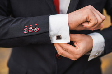 Elegant young fashion man dressing up for wedding celebration. Color close up image of male hands. Handsome groom dressed in modern black formal suit, white shirt and tie getting ready for event.