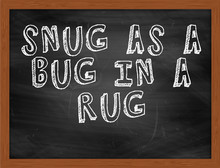 SNUG AS A BUG IN A RUG Handwritten Text On Black Chalkboard