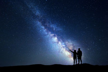 Milky Way With People On The Mountain. Landscape With Night Sky With Stars And Silhouette Of Standing Happy Man And Woman Who Pointing Finger In Starry Sky. Blue Milky Way. Galaxy. Bright Stars