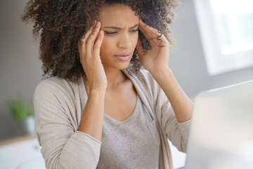 Wall Mural - Mixed race woman having a headache working on laptop