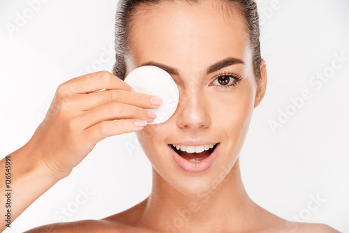 Poster Laughing woman holding round white cotton pad to her eye