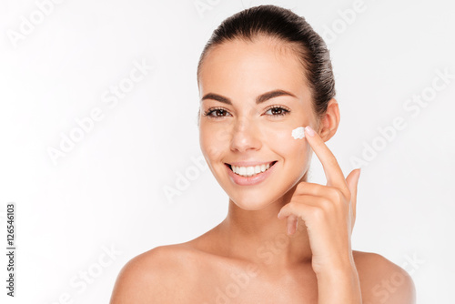 Fotografie, Obraz Beautiful young woman applying cosmetic cream treatment on her face